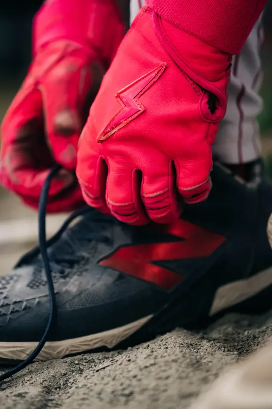 Red batting gloves pull a cleat lace tight.