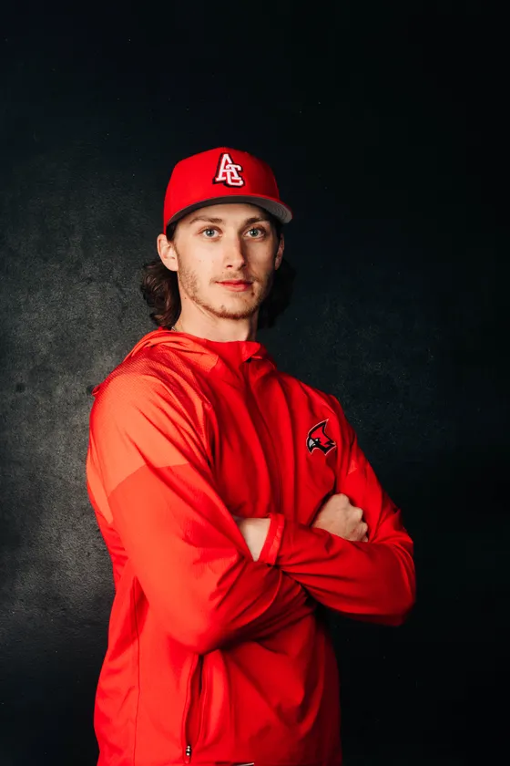 A Cardinals player in a red warm-up jacket stands against a dark studio backdrop.