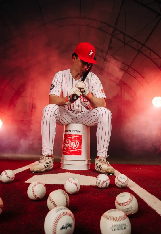 A Cardinals player sits with his bat under the red lights of the training dome.