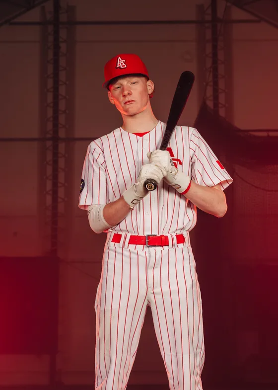 An Abbotsford Cardinals hitter holds his bat high in a red-lit studio portrait.