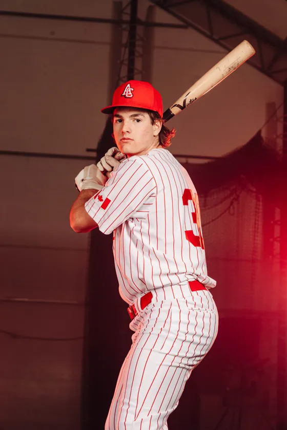 An Abbotsford Cardinals hitter sets his stance under red studio light.